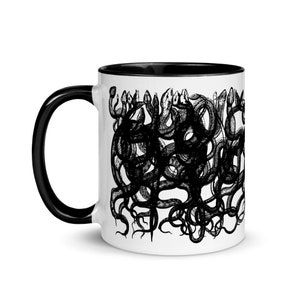 May include: White ceramic coffee mug with a black rim and handle. The mug features a black and white illustration of a group of snakes intertwined.