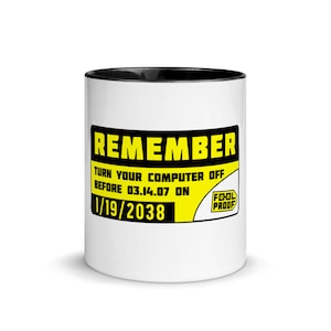Può includere: Tazza in ceramica bianca con bordo nero. La tazza presenta un cartello di avvertimento giallo e nero che recita "REMEMBER TURN YOUR COMPUTER OFF BEFORE 03.14.07 ON 1/19/2038 FOOL PROOF".