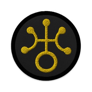 May include: A black and gold embroidered patch with a stylized symbol of a circle with four arms extending from it.