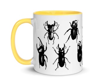 Puede incluir: Taza de cerámica blanca con borde amarillo. La taza presenta una ilustración en blanco y negro de seis tipos diferentes de escarabajos.