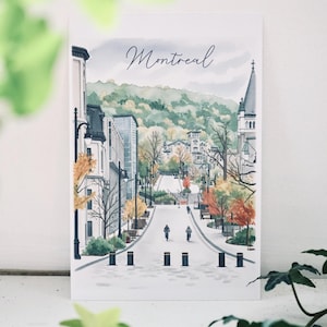 May include: A rectangular art print featuring a watercolor illustration of a Montreal street scene. The image depicts a sloping road with trees in autumn colors, buildings, street lamps, and two cyclists. The word Montreal is written in script.