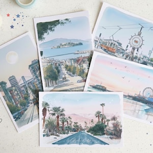 May include: A collection of five rectangular postcards featuring watercolor-style illustrations of various California landmarks, including city streets, a pier with a Ferris wheel, palm trees, and a bay view with an island, all with soft pastel colors.