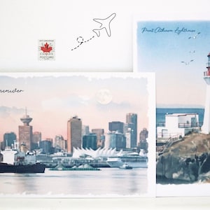 Könnte beinhalten: Zwei rechteckige Postkarten mit Aquarellillustrationen. Eine zeigt die Skyline von Vancouver bei Sonnenuntergang mit Mond, die andere den Point Atkinson Leuchtturm am Meer. Eine kleine Canada Postcard Briefmarke und ein Flugzeug sind zu sehen.