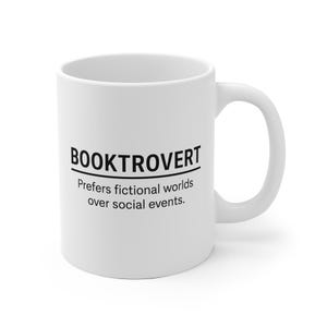 Könnte beinhalten: Weiße Keramiktasse mit dem schwarzen Wort "BOOKTROVERT" und dem Text "Bevorzugt fiktive Welten gegenüber gesellschaftlichen Ereignissen". Die Tasse hat einen gebogenen Henkel und ist für heiße oder kalte Getränke geeignet.
