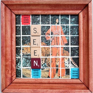 Puede incluir: Una obra de arte enmarcada con la palabra "SEEN" deletreada con fichas de Scrabble. El fondo es un collage con una mujer con un atuendo naranja y un leopardo. El marco es de madera marrón rojiza.