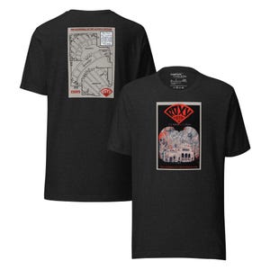 May include: Dark gray t-shirt featuring a graphic of the Roxy Theater. The front of the shirt displays a vintage poster design with the theater's name and architectural details. The back of the shirt has a map of the theater.