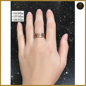 May include: A hand wearing two rose gold rings with a braided design. The rings are on the ring finger. The image also includes text that reads "144 Mhz", "177 Mhz", and "188 Mhz".