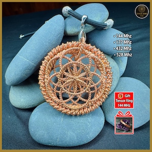 May include: A copper-colored pendant with a woven design, suspended from a black cord with silver-toned accents. The pendant rests on gray stones. Text on the image includes frequency measurements: 144 Mhz, 177 Mhz, 432 Mhz, and 528 Mhz.