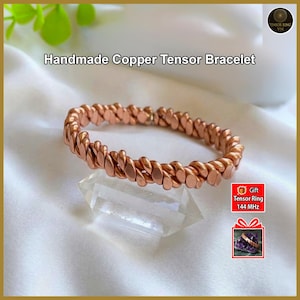 Könnte beinhalten: Ein handgefertigtes Kupfer-Tensor-Armband mit einem gedrehten Design. Das Armband hat eine warme Kupferfarbe und liegt auf einem klaren Kristall. Der Text "Handmade Copper Tensor Bracelet" wird über dem Armband angezeigt.