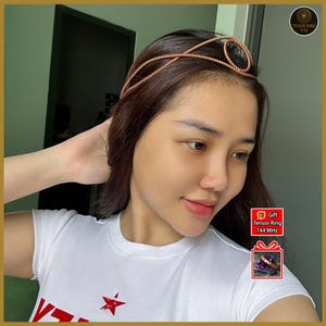May include: A copper-colored Tensor Ring headband with a spiral design. The headband is worn on the head. The person is wearing a white t-shirt with a red star graphic. The image also includes a gift box with the text "Tensor Ring 144 MHz".