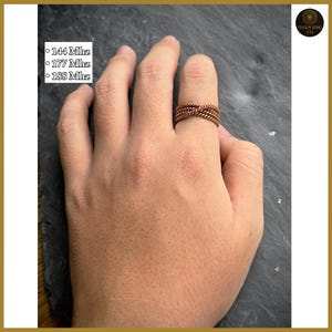 Può includere: Un anello color rame con un design intrecciato è indossato su un dito. L'anello è realizzato con più fili di metallo attorcigliati. Il testo sul lato sinistro dell'immagine recita: 144 Mhz, 177 Mhz e 188 Mhz.