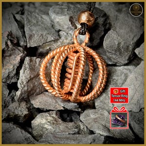 May include: A copper-colored pendant necklace with a unique, intertwined design. The pendant features three circular elements and a central, vertical bar. The necklace hangs from a black cord. The image includes the text "Gift Tensor Ring 144 MHz".