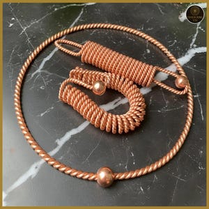 May include: A set of copper-colored tensor rings and a tensor coil, displayed on a black marble surface. The set includes a large ring, a smaller ring, and a coil, all made of twisted copper wire. The rings each have a copper sphere.