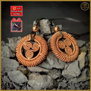 Peut inclure: Deux colliers pendentifs cuivrés avec un motif en spirale, présentés sur un lit de roches grises. Chaque pendentif a un cadre circulaire avec un motif en spirale interne. Les colliers sont suspendus à des cordons noirs.