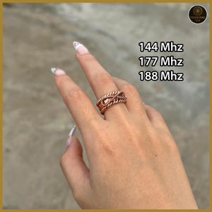 May include: A copper-colored ring featuring a braided, rope-like texture. The image includes text reading 144 Mhz, 177 Mhz, and 188 Mhz, along with a circular logo in the corner labeled Tensor Ring VN. The ring has a wide, multi-strand design.