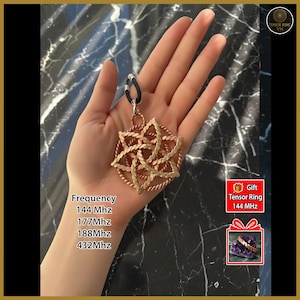 May include: A copper-colored pendant with a geometric design, held in a hand. The pendant is suspended from a black cord. Text on the image includes frequency measurements: 144 Mhz, 177 Mhz, 188 Mhz, and 432 Mhz. A gift box graphic is also present.