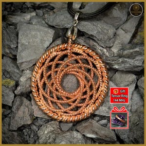 May include: Copper-colored pendant necklace with a spiral design. The pendant is suspended from a black cord. The background is composed of gray rocks. The image includes a gift box graphic with the text "Tensor Ring 144 MHz".