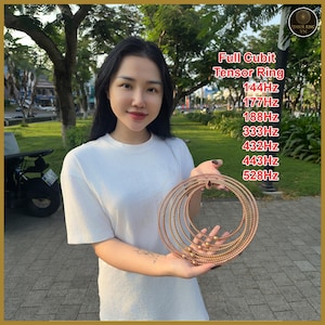 Puede incluir: Una mujer sostiene un conjunto de anillos Tensor de color cobre. Los anillos están dispuestos en círculos concéntricos, con el anillo más grande de aproximadamente 25 cm de diámetro. El texto en la imagen dice "Full Cubit Tensor Ring" y enumera frecuencias.