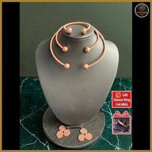 Pode incluir: Um conjunto de joias de cor cobre exposto em um manequim. O conjunto inclui um colar, uma pulseira e brincos. O colar e a pulseira têm um design de corda torcida com detalhes esféricos. Os brincos têm um design em espiral.