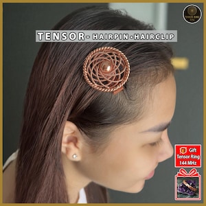 Könnte beinhalten: Ein kupferfarbener Tensor-Haarspange oder Haarclip. Das Haaraccessoire hat ein kreisförmiges Design mit einem Spiralmuster und einer zentralen Perle. Der Text "Tensor - Hairpin - Hairclip" wird darüber angezeigt.