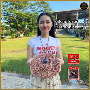 May include: A 63cm Torus Harmoniser featuring a spherical purple crystal at the center of a coiled copper wire structure. The object is suspended on a black cord. Text on the image reads 63cm Torus Harmoniser and Gift Tensor Ring 144 MHz.