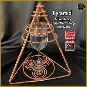 Op de afbeelding: Een koperen piramidestructuur met een glas water erin. De piramide is gemaakt van gedraaide koperdraad en heeft een driehoekige basis. Tekst op de afbeelding luidt "Pyramide 6-Frequentie Koperen Waterlader Energietool".