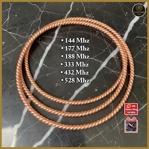 May include: Copper-colored Tensor Rings, each with a twisted rope design, are arranged in a nested pattern. The rings are labeled with frequencies: 144 Mhz, 177 Mhz, 188 Mhz, 333 Mhz, 432 Mhz, and 528 Mhz. The background is a dark marble.