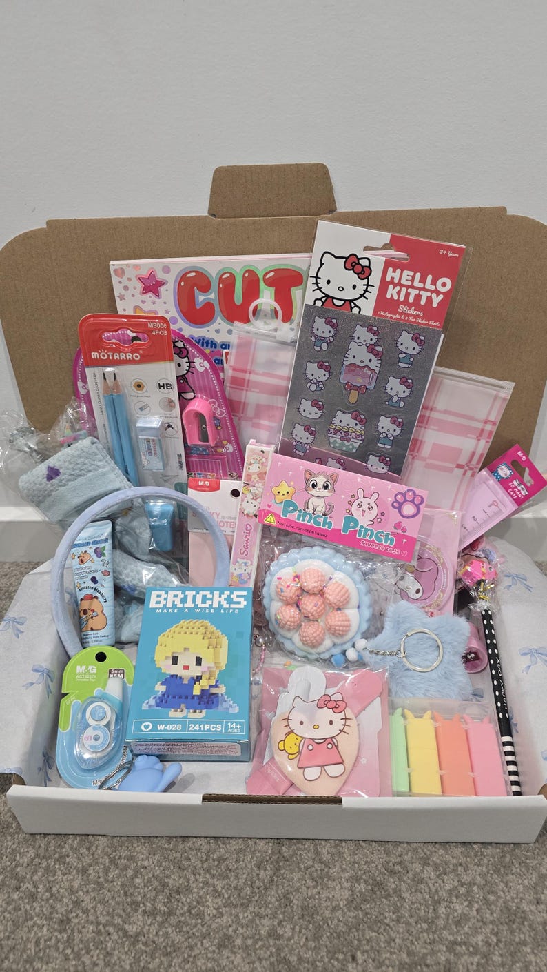 May include: A gift box filled with various stationery and accessories. Items include Hello Kitty stickers, pencils, a blue headband, a small building block set, and a variety of other pink and blue items. The box is open, revealing the contents.