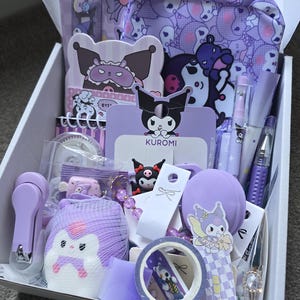 May include: A white box filled with purple Kuromi-themed stationery and accessories. Items include a pencil case, stickers, pens, a ruler, washi tape, and a nail clipper. The box is open, revealing the contents inside.