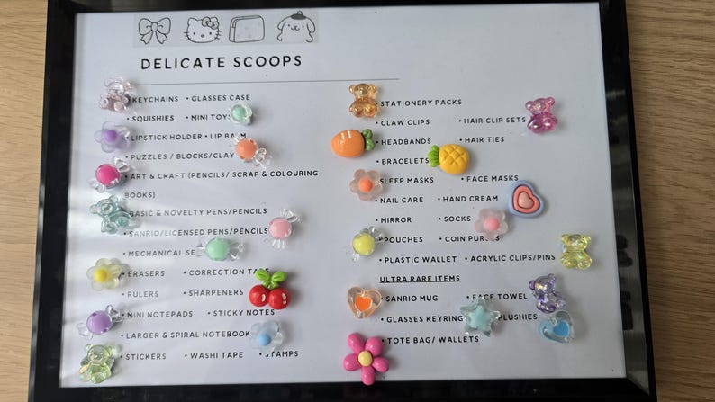 May include: A framed display featuring various small, colorful accessories. The items include keychains, squishies, and hair clips, along with other stationery and novelty items. The text "DELICATE SCOOPS" is at the top.