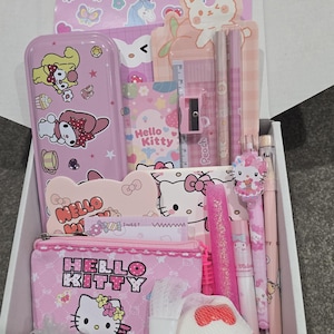 May include: A pink Hello Kitty themed gift box filled with stationery items. Includes a pencil case, pencils, pens, a ruler, a pencil sharpener, and stickers. The box is filled with pink and white items.