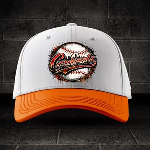 May include: A white baseball cap with an orange brim. The front features a graphic of a baseball with a red and black stylized script that reads Cardinals, surrounded by a distressed, paint-splatter effect in shades of red, black, and orange.