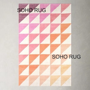 Puede incluir: Alfombra rectangular con un patrón geométrico de triángulos en tonos rosa, naranja y blanco. El texto "SOHO RUG" está impreso en la alfombra. La alfombra tiene un efecto degradado, pasando del morado oscuro al melocotón claro.