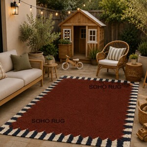 Pu&ograve; includere: Un tappeto rettangolare con un centro rosso scuro e un bordo di zigzag blu navy, bianchi e neri alternati. Le parole "SOHO RUG" sono stampate sul tappeto. Il tappeto &egrave; posizionato su un patio con mobili da esterno.