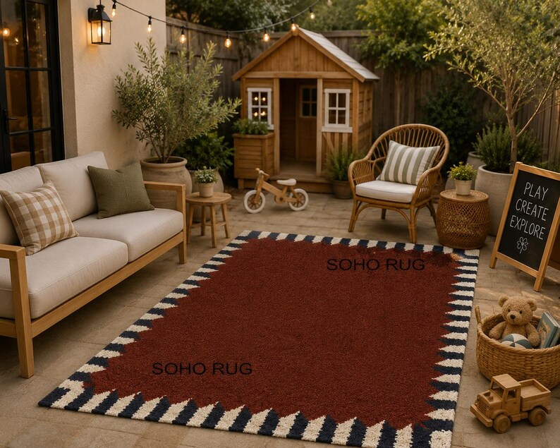 Pu&ograve; includere: Un tappeto rettangolare con un centro rosso scuro e un bordo di zigzag blu navy, bianchi e neri alternati. Le parole "SOHO RUG" sono stampate sul tappeto. Il tappeto &egrave; posizionato su un patio con mobili da esterno.