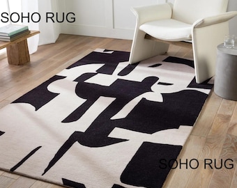 May include: A rectangular rug with a striking black and white abstract pattern. The rug displays large, geometric shapes in black against a white backdrop. The words "SOHO RUG" are printed on the rug.