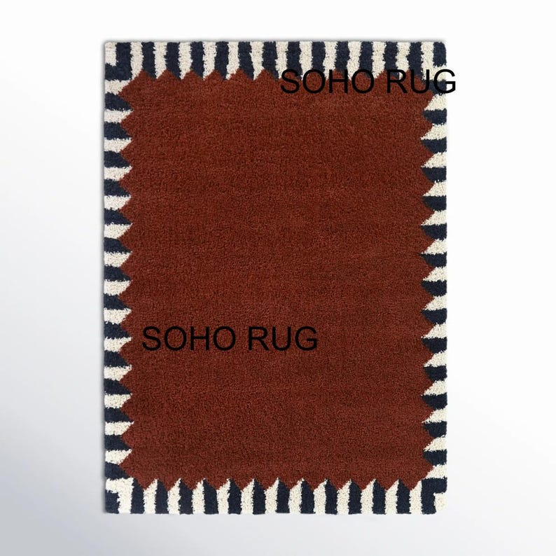 Pu&ograve; includere: Un tappeto rettangolare con un centro marrone scuro e un bordo di strisce verticali blu navy e bianche alternate. Il testo "SOHO RUG" &egrave; stampato sul tappeto. Il tappeto &egrave; su sfondo bianco.