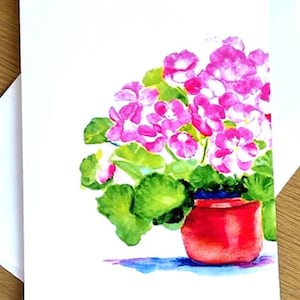Puede incluir: Pintura a la acuarela de una planta en maceta con flores rosas vibrantes y hojas verdes. La maceta roja se asienta sobre una superficie azul, todo sobre un fondo blanco. La obra de arte está en una tarjeta blanca.