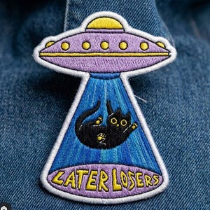 May include: Embroidered patch featuring a purple UFO with yellow accents, beaming up a black cat. The patch has a blue beam and the text "ZATER LOSERS" in yellow.