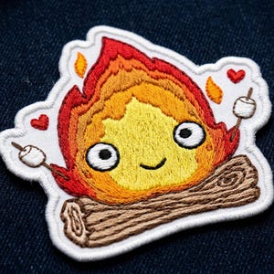 May include: Embroidered patch featuring a smiling campfire with flames in shades of red, orange, and yellow. The campfire has a log base and holds two marshmallows on sticks, with small red hearts. The patch has a white border.