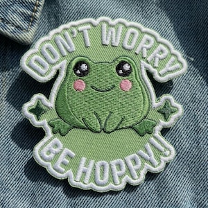 May include: Embroidered patch featuring a smiling green frog with the text "DON'T WORRY BE HOPPY" in white. The frog has black eyes and pink cheeks. The patch is outlined in white and has a star on each side.