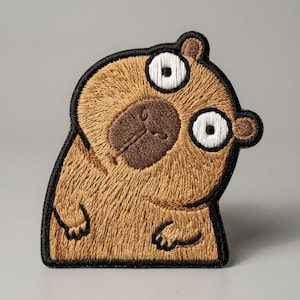 May include: Embroidered patch featuring a cartoon capybara with a surprised expression. The patch has a brown body, a dark brown face, and large white eyes with black pupils. The capybara is outlined in black.