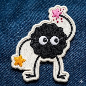 May include: Embroidered patch featuring a black, round creature with large white eyes and small legs. The patch has a white border and includes a yellow star and a pink star with red dots. The patch is on a blue denim background.