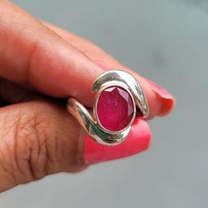 May include: A silver ring with a large, round, red gemstone set in a curved band.