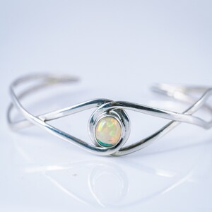 May include: A silver bracelet with a delicate, interwoven design features a white opal gemstone in the center.