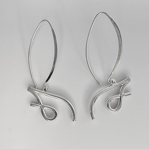 May include: A pair of silver dangle earrings with a unique abstract design. The earrings are made of thin, curved wire and have a simple, modern look.