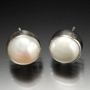 May include: A pair of silver stud earrings with white pearl accents.