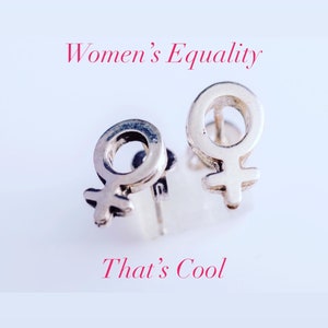 K&ouml;nnte beinhalten: Zwei silberne Ohrringe in Form des weiblichen Geschlechtszeichens. Die Ohrringe befinden sich auf einem wei&szlig;en Hintergrund. Der Text "Women's Equality" befindet sich &uuml;ber den Ohrringen und der Text "That's Cool" unter den Ohrringen.
