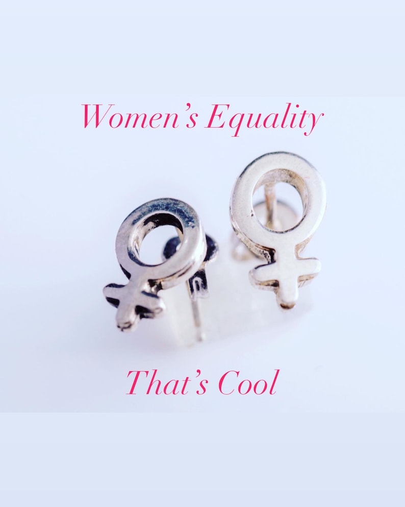 K&ouml;nnte beinhalten: Zwei silberne Ohrringe in Form des weiblichen Geschlechtszeichens. Die Ohrringe befinden sich auf einem wei&szlig;en Hintergrund. Der Text "Women's Equality" befindet sich &uuml;ber den Ohrringen und der Text "That's Cool" unter den Ohrringen.