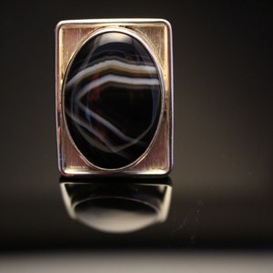 May include: A silver ring with a black and white agate stone set in a gold-toned frame.